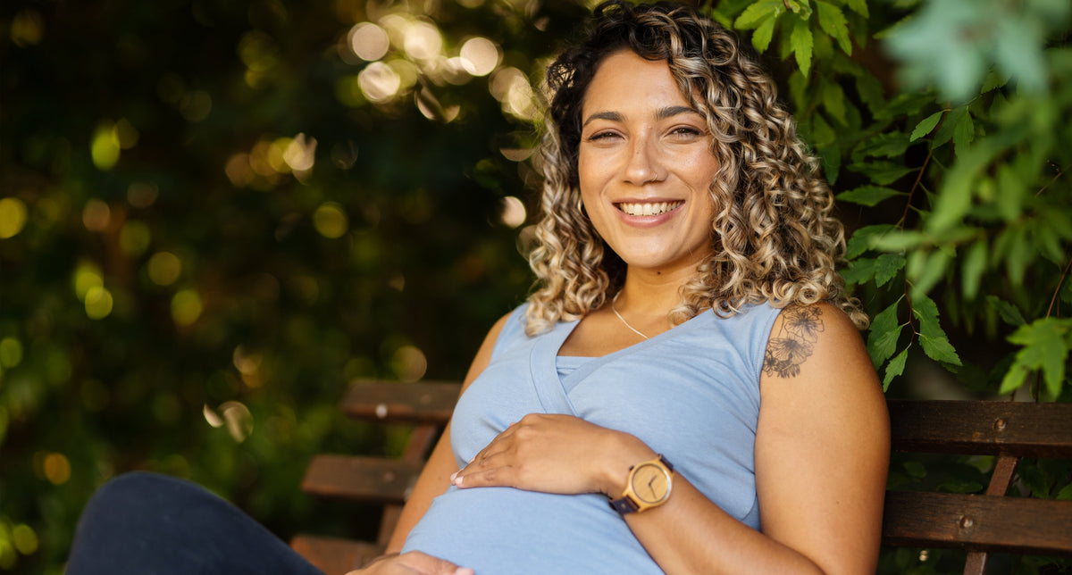 A pregnant woman sitting outdoors on a bench, one hand resting on her bump